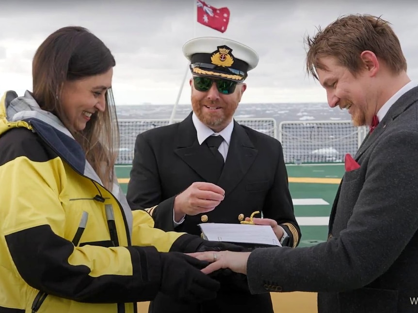 A bride and groom share rings while a ship captain officiates.
