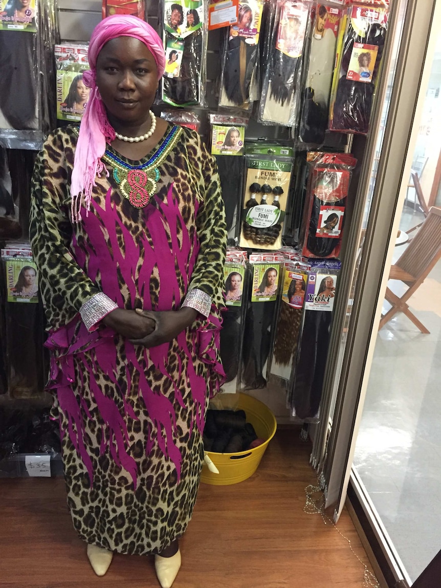 Grace Wani stands in traditional Sudanese dress, in front of some hair products