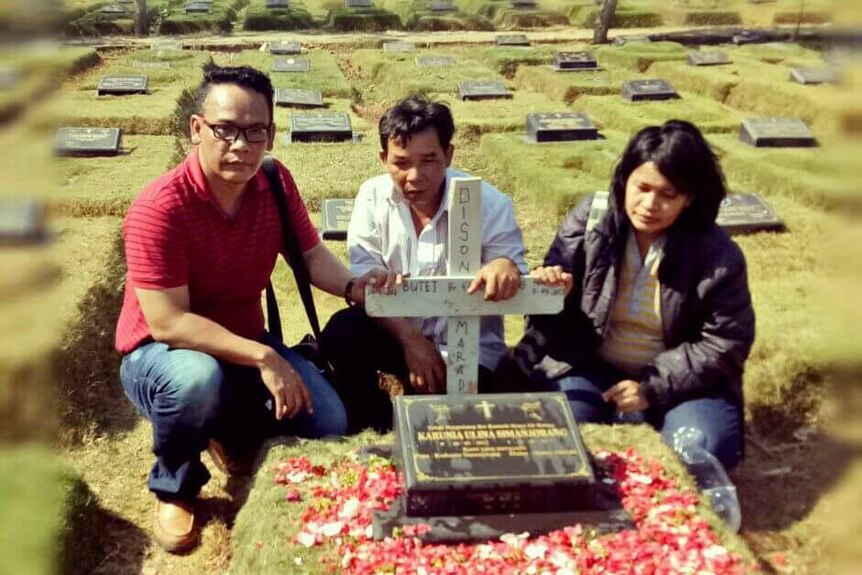 Henny Silalahi and Rudianto Simanjorang at Deborah's grave. It's a small plaque with a cross, covered in flower petals.
