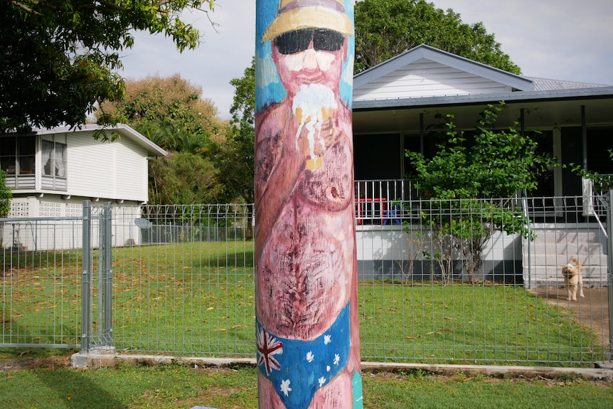 A power pole painted with a picture of a burly shirtless man eating an icecream