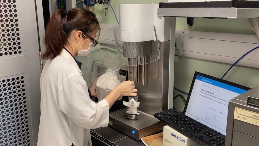 Women in lab coat and protective goggles holding sugar under a microscope. 