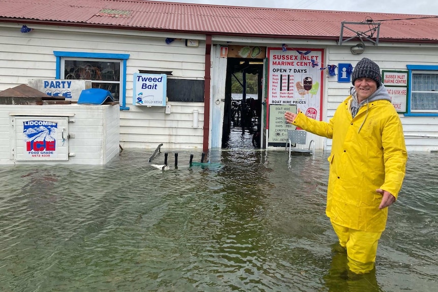 A man stands outside a flooded shopfront.