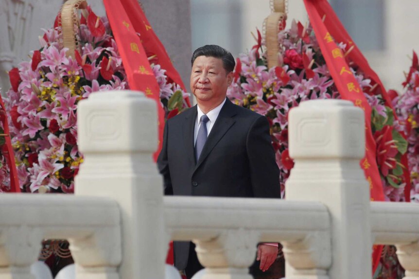 Chinese President Xi Jinping walks with a decorative rail in the foreground and flowers in the background.