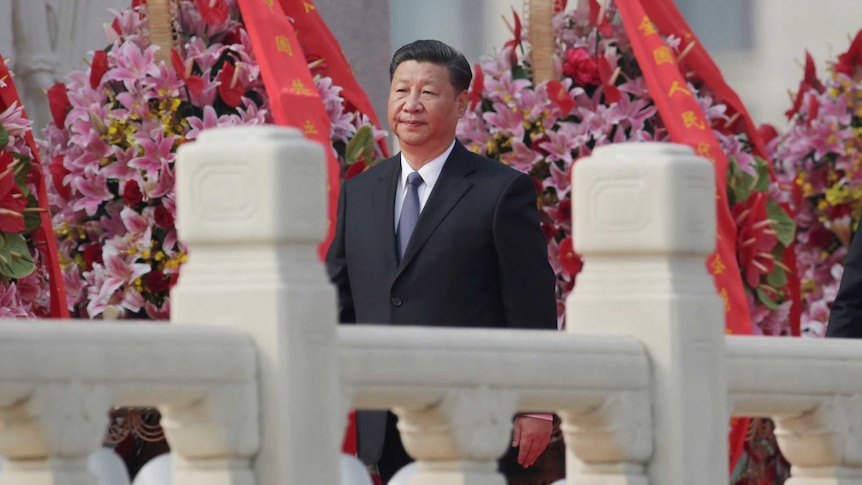 Chinese President Xi Jinping walks with a decorative rail in the foreground and flowers in the background.