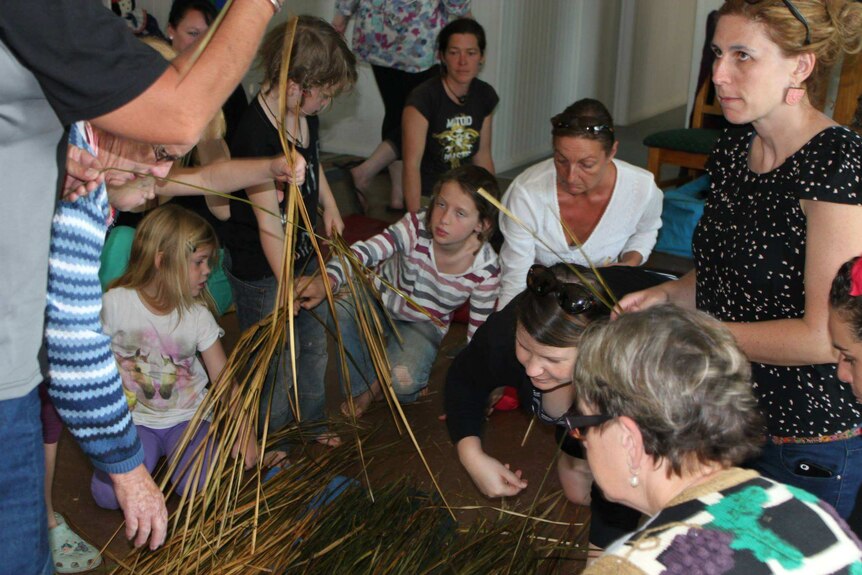 Women and children gather grass to weave into a basket.