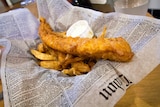 A fried fish and chips in a news paper basket.