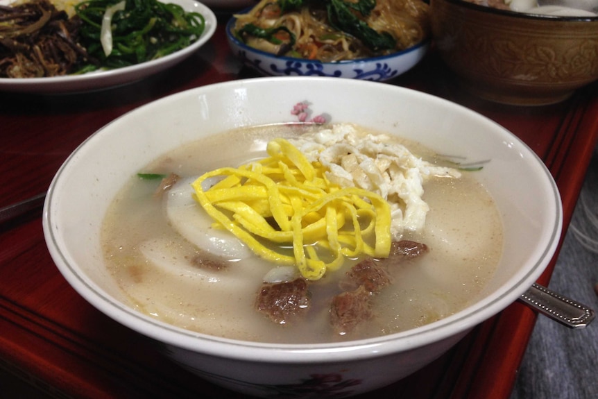 Rice cake soup in a bowl surrounded by other banquet dishes.