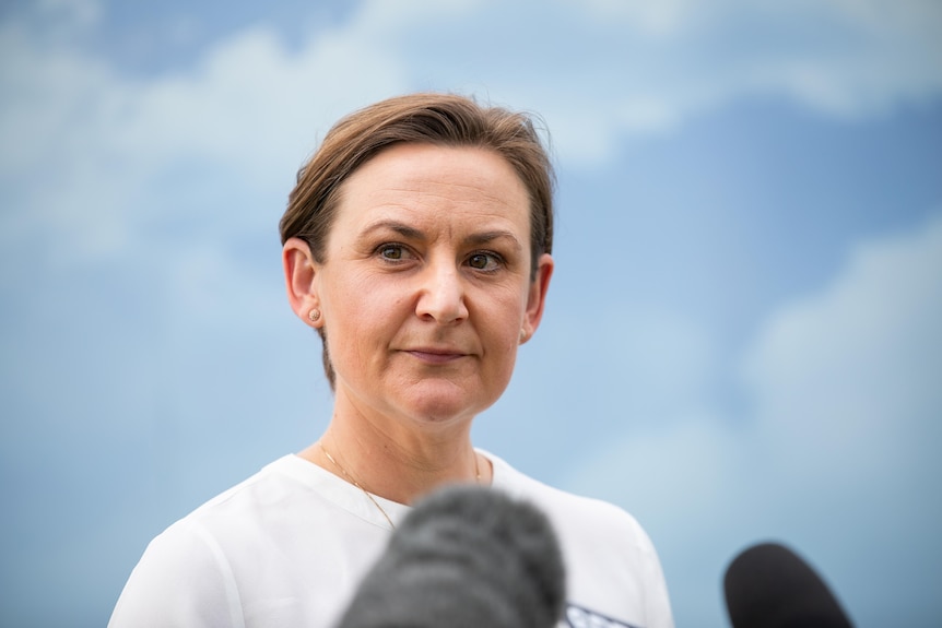 A woman with short hair standing in front of microphones and looking to the side.