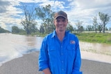 A farmer in a blue shirt stands in front of floodwater
