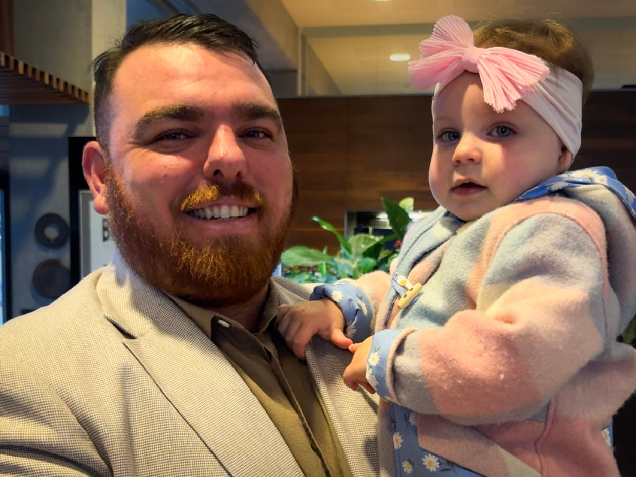 A man with a beard holds a little girl with a bandana around her head.