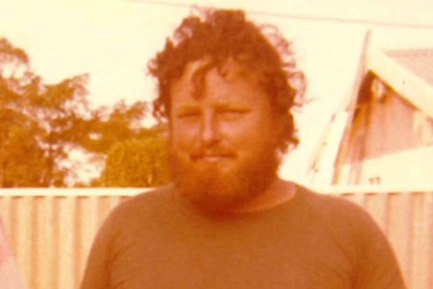 An old photo of Terence John Fisher in the yard of a house holding a drink in a glass, with bushy hair and a bushy beard.