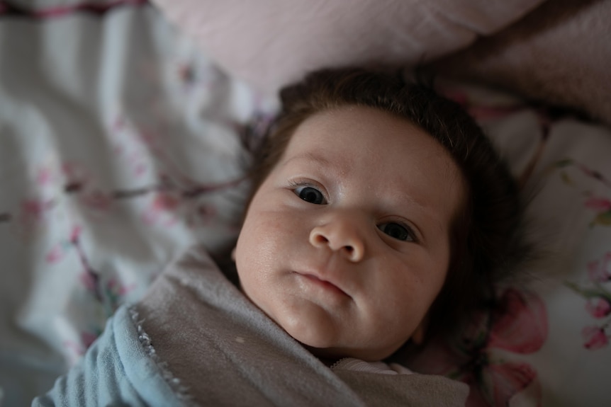 A baby boy, a few months old, looks up at the camera. He has thick brown hair.