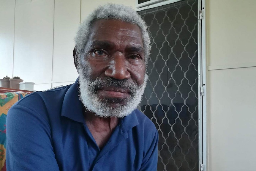 Bill Cletus Jakanduo sits on a front porch in front of a wire door