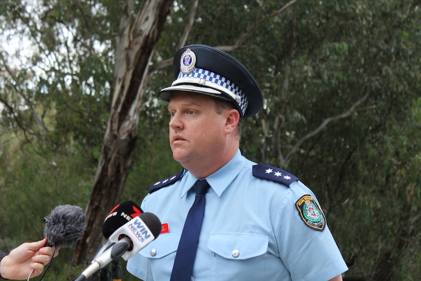 A uniformed policeman stands outside, taking questions from the media.