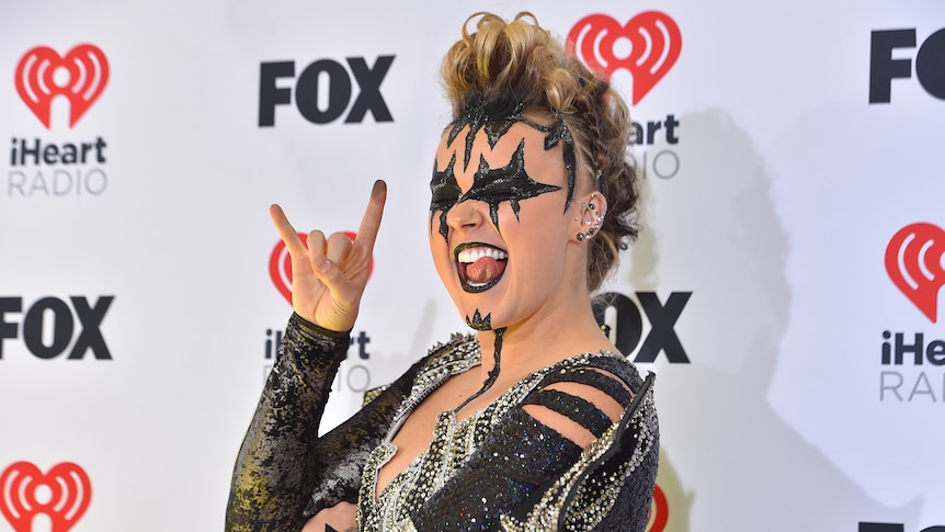 JoJo Siwa poses wearing a black and silver outfit and with black paint decorating parts of her face.