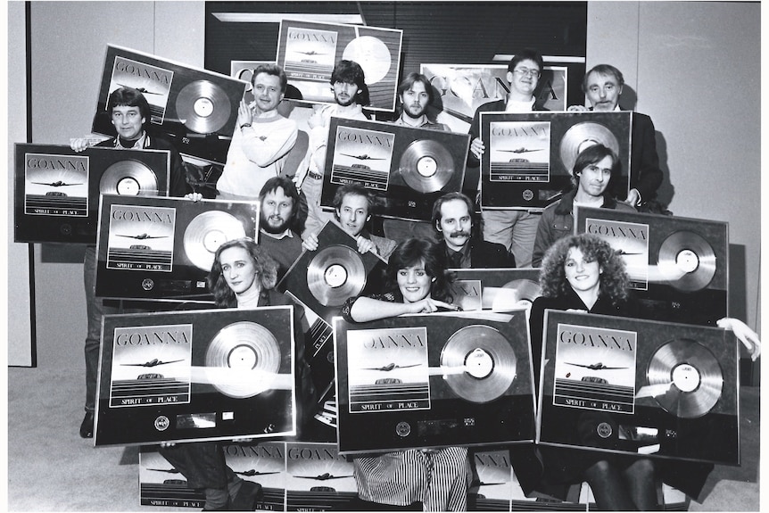 A group of people hold up platinum records, marking 70,000 albums sold