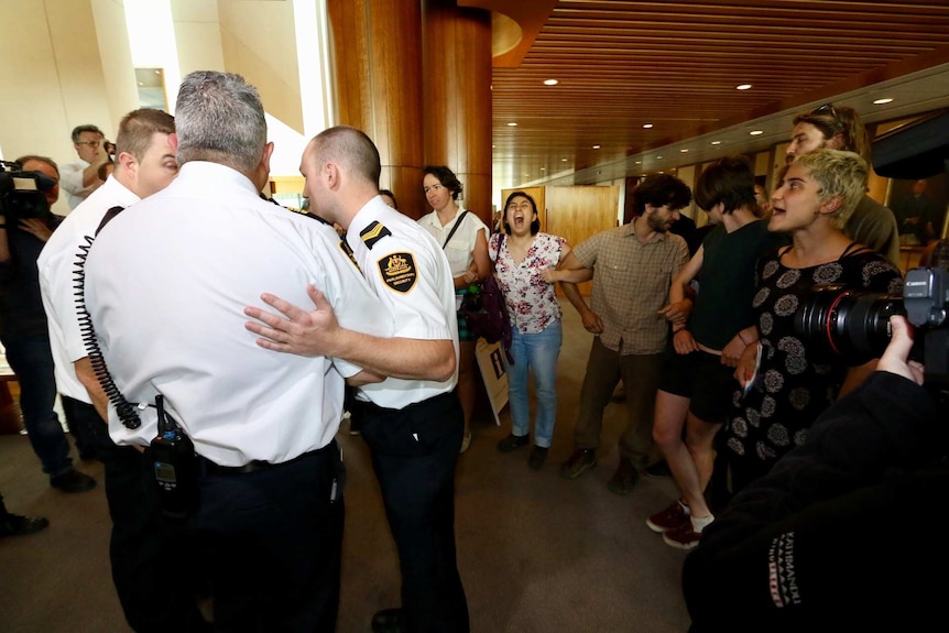 A group of anti-offshore detention protesters link arms and yell at Parliament House security guards.
