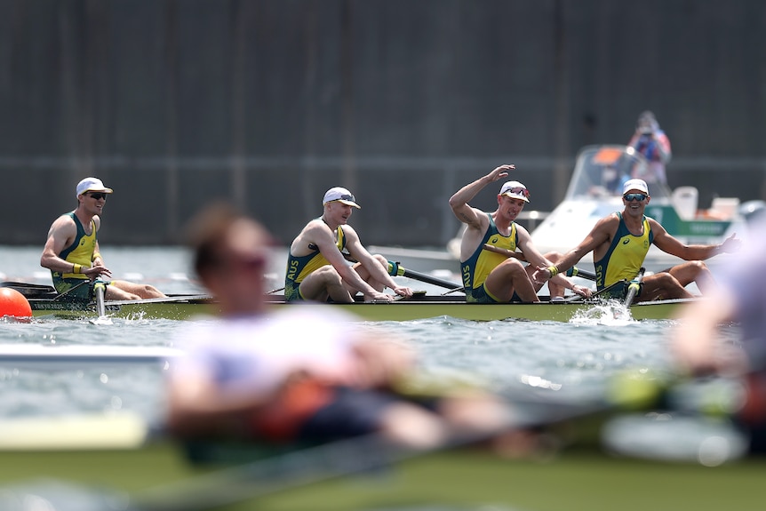 Four men in a boat raise their arms in the air