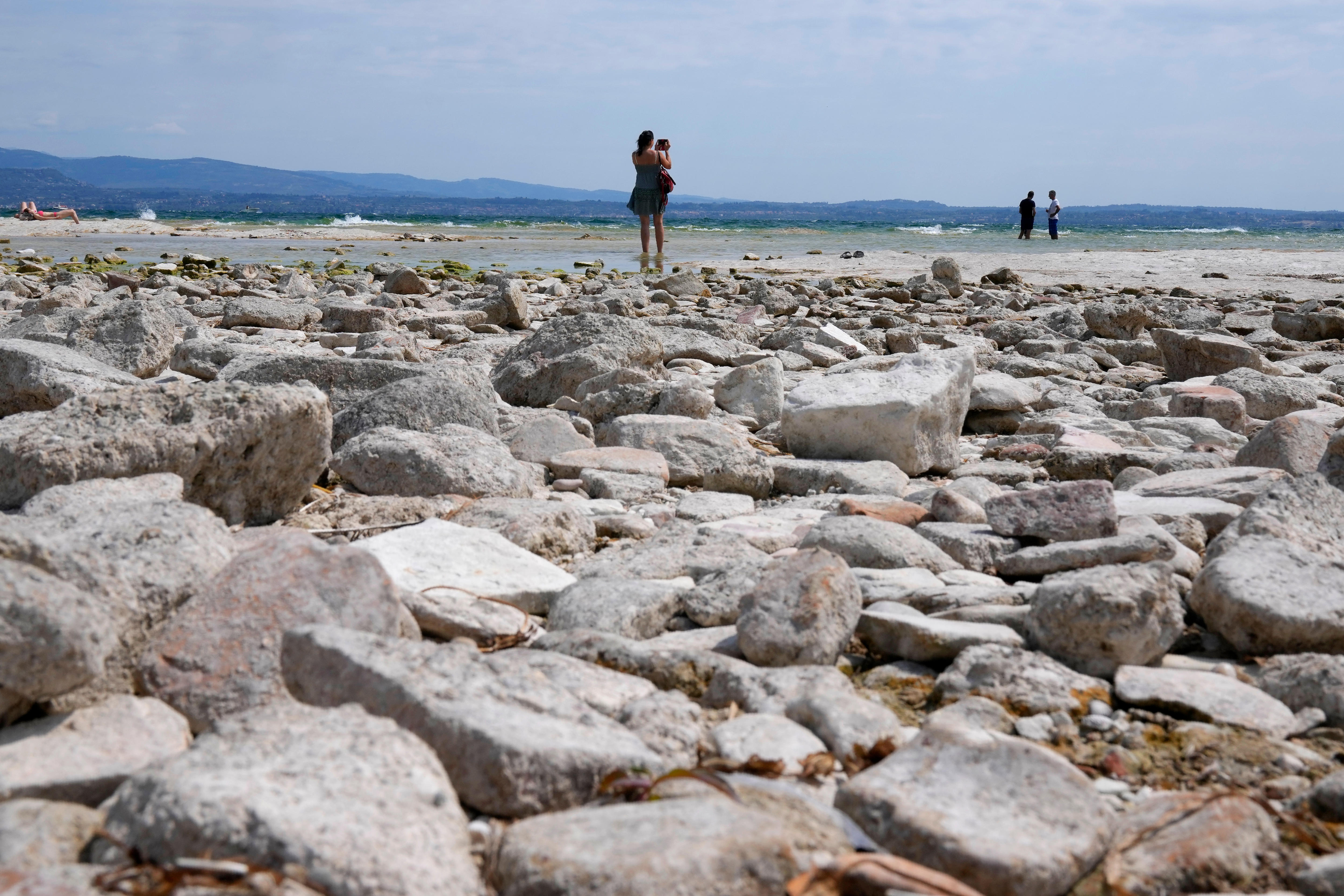 A woman holds a child while walking on rocks at Lake Garda
