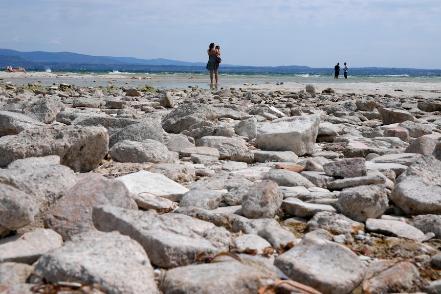 A woman holds a child while walking on rocks at Lake Garda