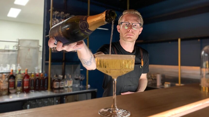 A bartender wearing glasses pours a non-alcoholic sparkling wine into a glass at Brunswick Aces