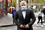 Stuart MacGill wearing a suit and a covid mask