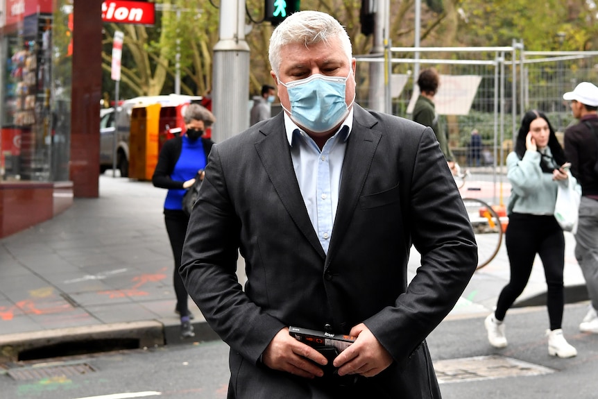 Stuart MacGill wearing a suit and a covid mask