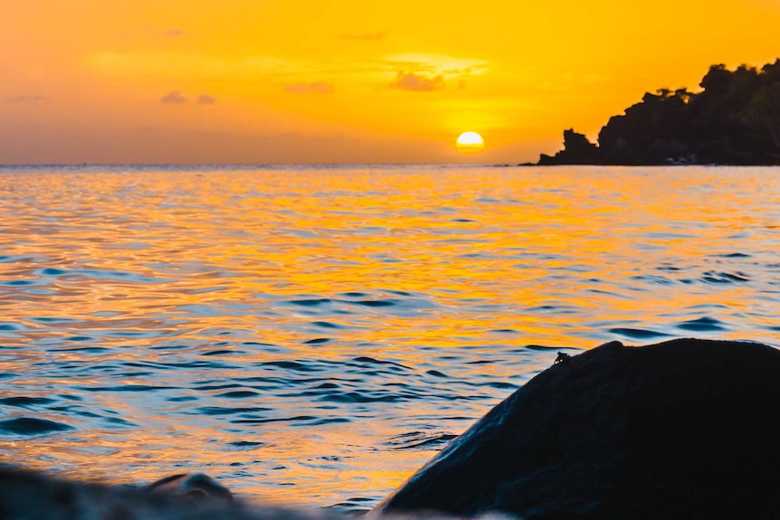 A sun setting over the sea near a tropical island.