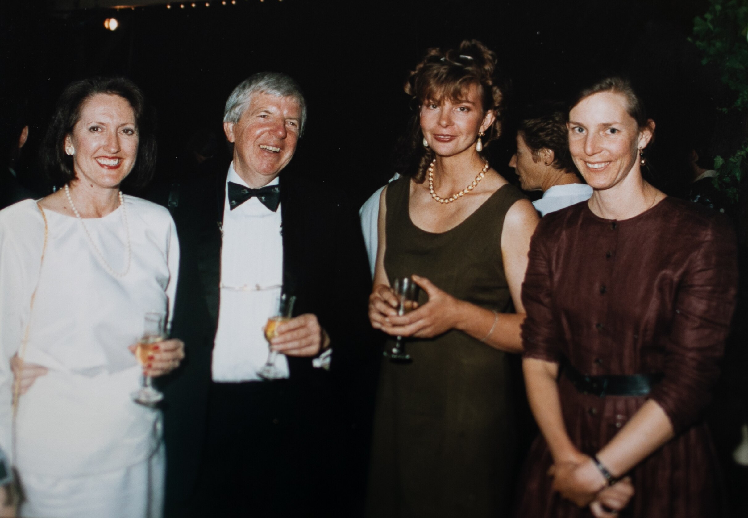 A 90s photograph of four adults in evening attire, woman second from right in sage green shift dress with hair in updo