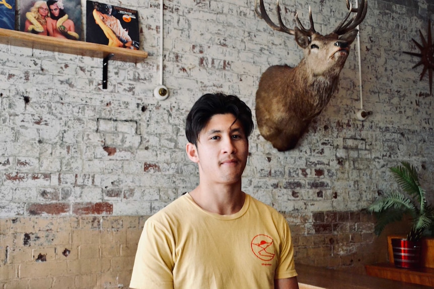 Man standing in bar with stag's head on wall behind him
