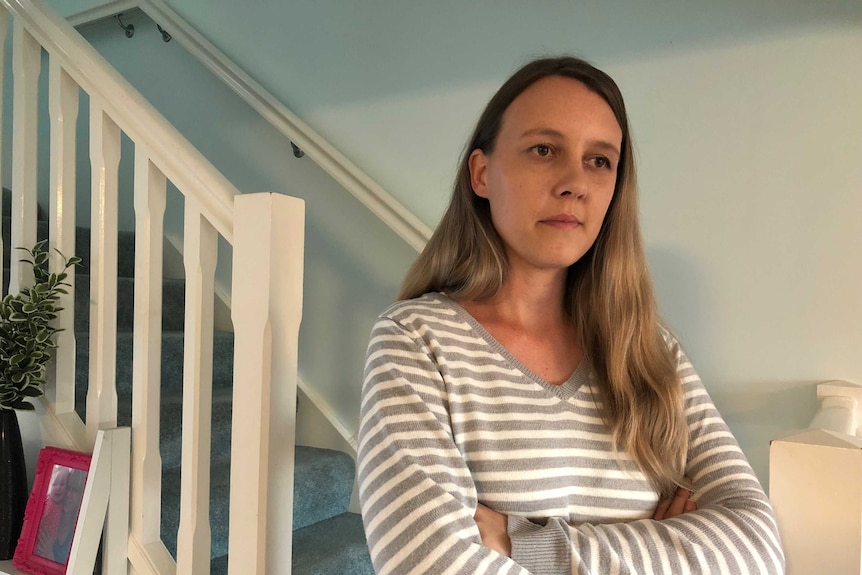 Woman stands at bottom of indoor stairs with family photo in background