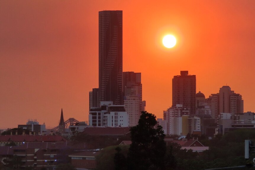 An orange sky glows over Brisbane, with the sun a deep shade of orange due to smoky haze.