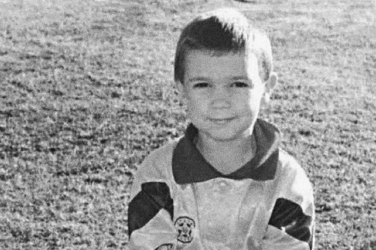 A grainy black and white photo of a young child wearing football jersey sitting on grass on sunny day.