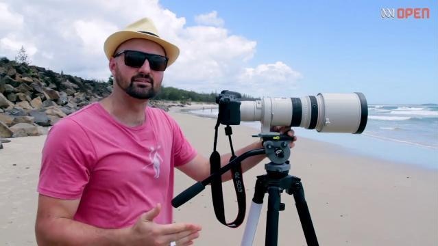 Man stands on beach with camera on tripod