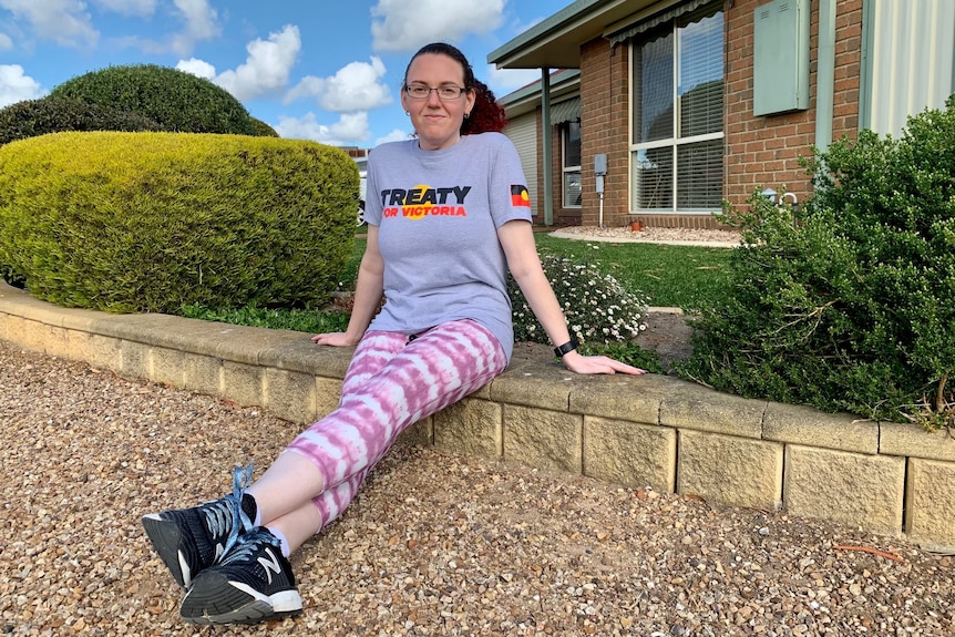 a woman sitting on a footpath wearing a tshirt that says 'treaty'