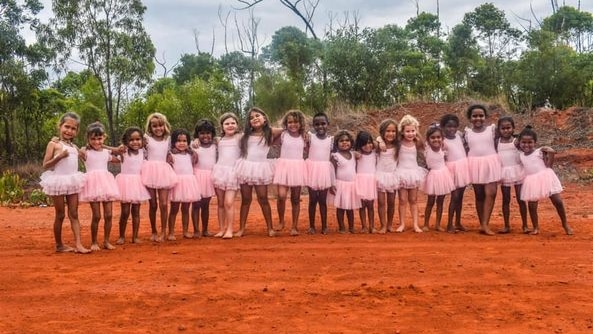 A group of young Aboriginal girls in pink costumes standing on red dirt