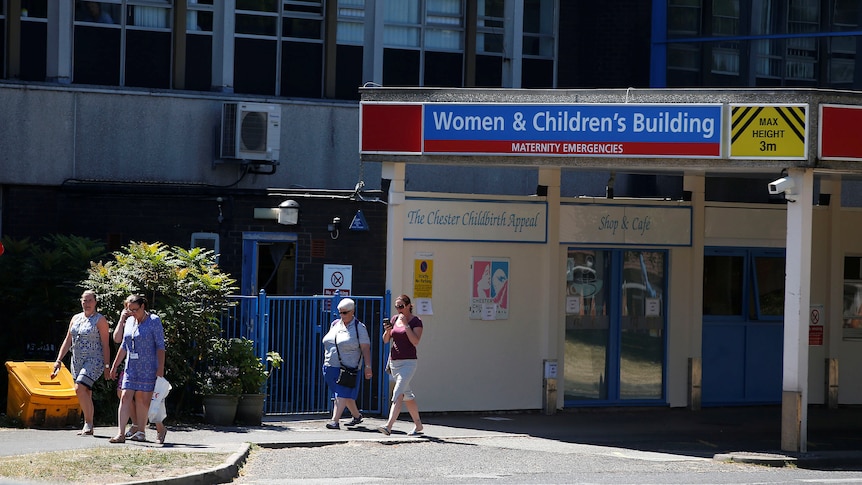 People walk out of a hospital entrance with a sign on top reading WOMEN'S AND CHILDREN'S BUILDING
