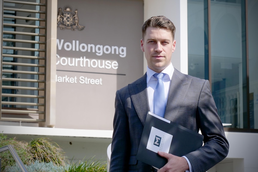 A man standing outside the Wollongong Courthouse wearing a suit holding a folder