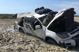 A four wheel drive heavily bogged in mud with its bonnet open and sleeping bags and gear on the roof.