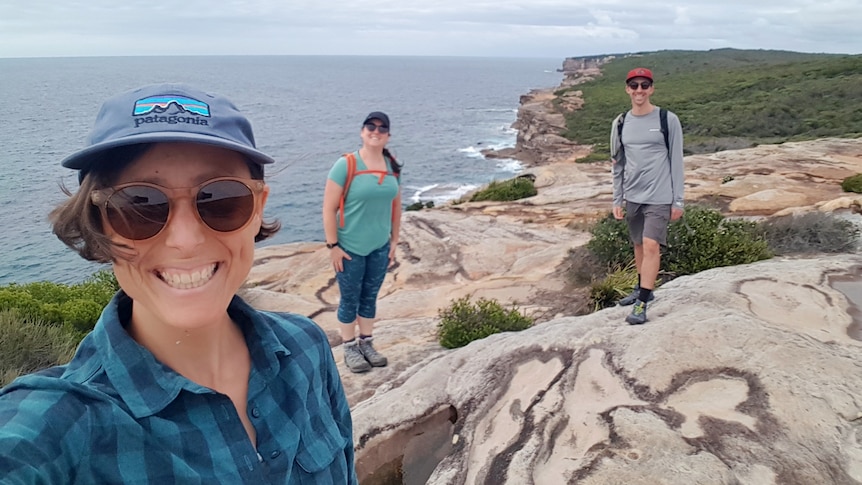 A woman stands near a cliff overlooking the sea, with friends in the background for a story on going off the contraceptive pill.