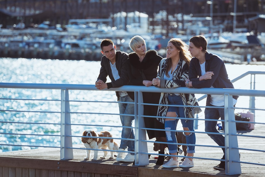 Tim Tszyu stands next to his mother Natalia and siblings, leaning on railings with water in the background