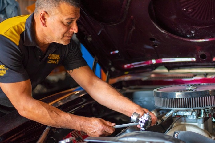 A mechanic working under a car bonnet on an engine.