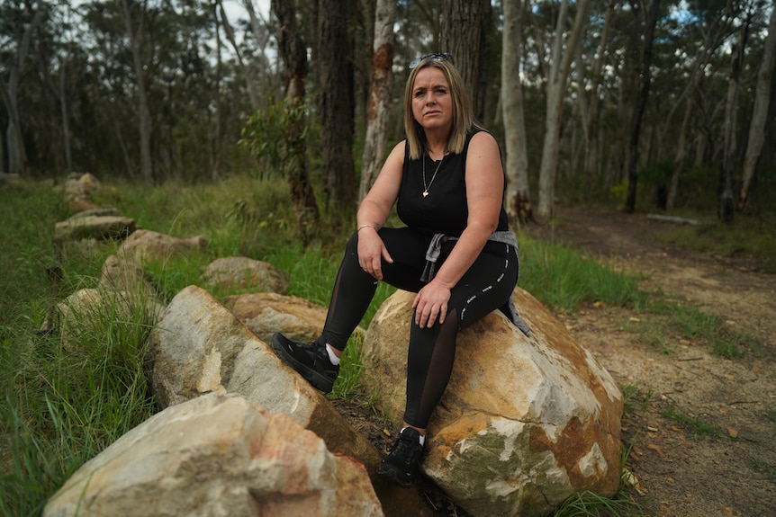 A woman sitting on a large rock in bushland.