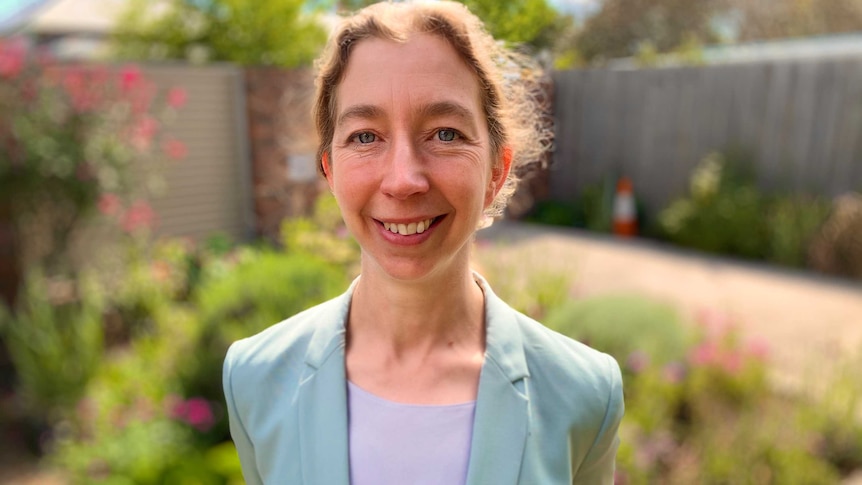 a woman in a blazer, smiling in a garden