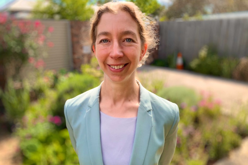 a woman in a blazer, smiling in a garden