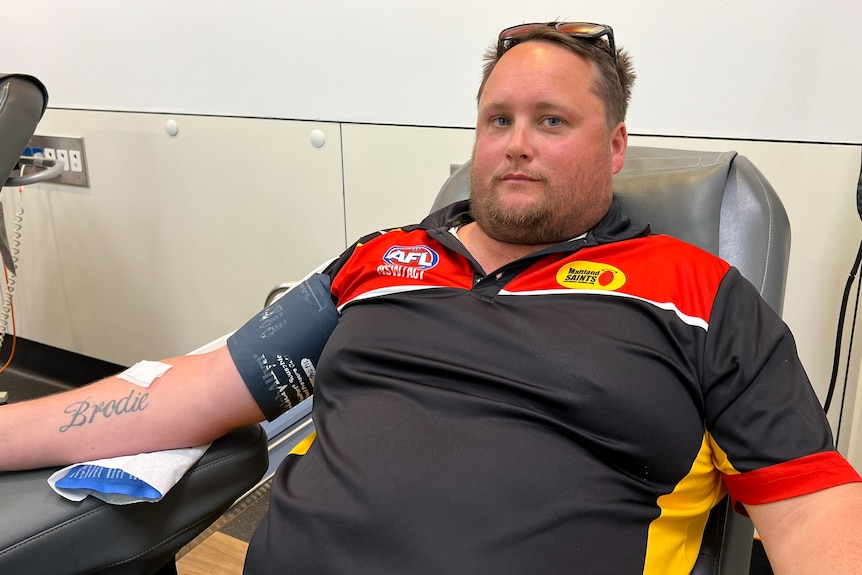 A young man sits in a chair donating blood.