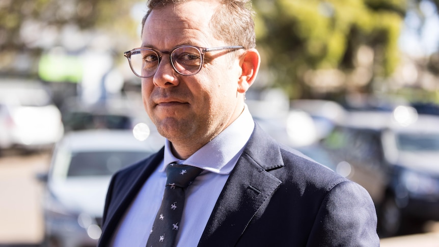 A bespectacled, middle-aged man in a dark suit walking towards a court building.