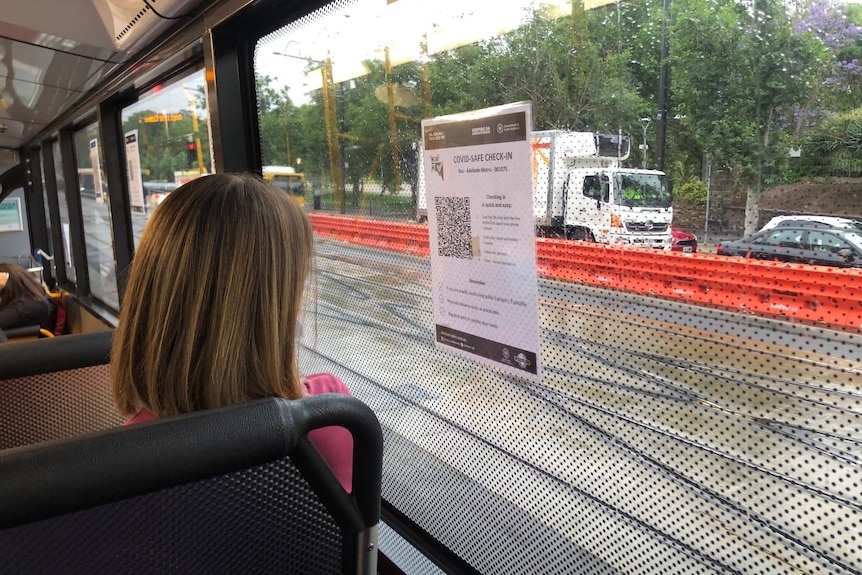 A piece of paper stuck to the inside of a bus window with a QR code on it with a woman looking out the window