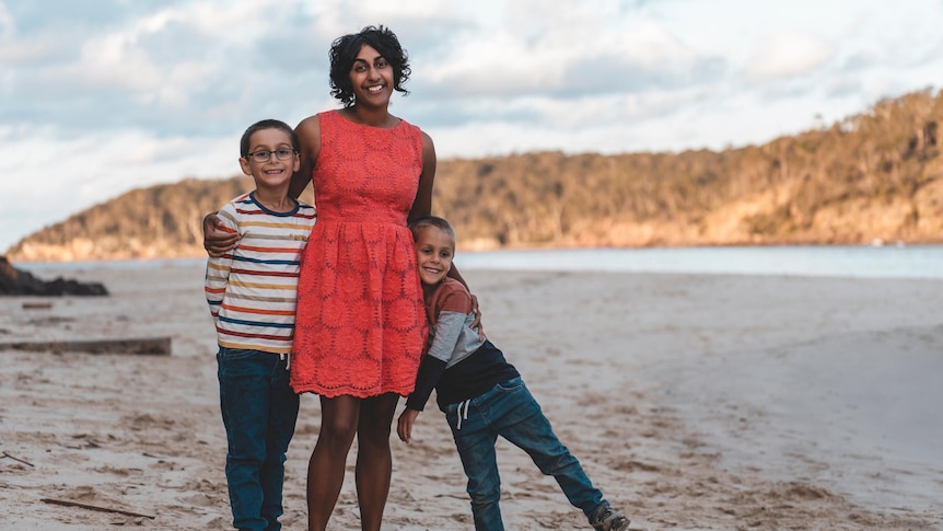 A woman in a pink dress with her two kids at a beach.