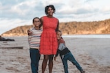 A woman in a pink dress with her two kids at a beach.